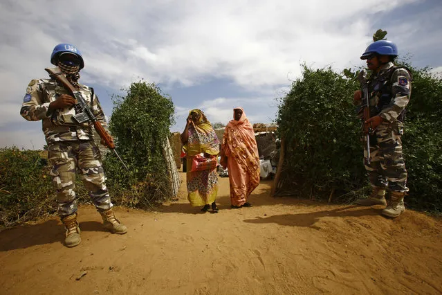 Women walk past UN peacekeepers standing guard at the Attash refugee camp in Nyala in South Darfur on January 9, 2017 following a visit by British senior officials overseeing a new cash assistance project implemented by the World Food Programme (WFP). (Photo by Ashraf Shazly/AFP Photo)