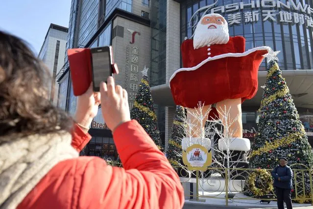 A woman takes a photo of a blow-up Santa Claus doll that imitates the famous Marilyn Monroe pose before a shopping mall in Taiyuan, central China's Henan province on December 11, 2013. Chinese inflation slowed to 3.0 percent in November to snap two months of acceleration in consumer prices, official figures showed, well under the government's target for the year, as analysts saw the result as largely positive for the world's second-largest economy, signalling no imminent need for authorities to tighten monetary policy. (Photo by AFP Photo)
