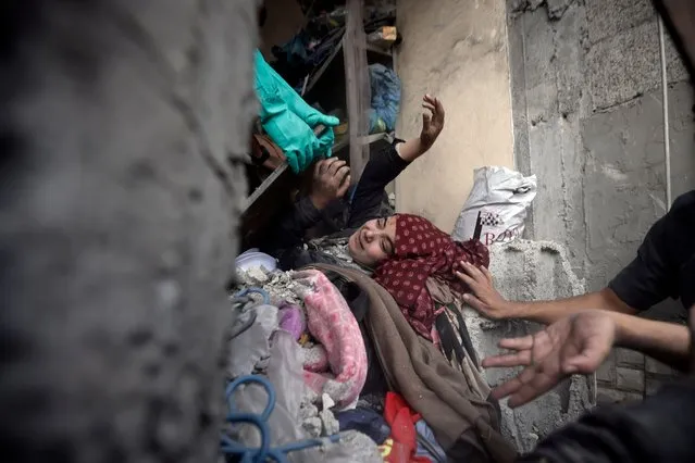 Palestinians try to rescue a woman stuck under the rubble of a destroyed building following Israeli airstrikes in Khan Younis refugee camp, southern Gaza Strip, Thursday, December 7, 2023. In recent days, Israeli tanks have rumbled into southern Gaza, starting with Khan Younis. (Photo by Mohammed Dahman/AP Photo)