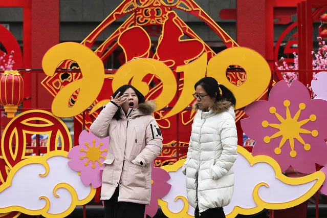 A woman yawns as she and her friend walk by a Lunar New Year decoration on display outside a commercial office building in Beijing, Thursday, January 31, 2019. China's manufacturing improved in January, a survey showed Thursday, but forecasters said activity remains sluggish as Beijing tries to resolve a tariff battle with Washington. (Photo by Andy Wong/AP Photo)