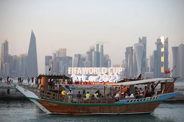 People ride a dhow past a FIFA World Cup sign in Doha on November 16, 2022, ahead of the Qatar 2022 World Cup football tournament. (Photo by Adrian Dennis/AFP Photo)