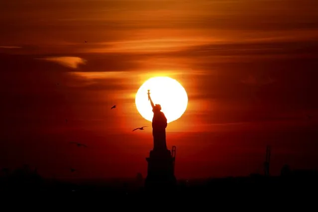 The sun sets behind the Statue of Liberty in New York's Harbor as seen from the Brooklyn borough of New York February 27, 2016. (Photo by Brendan McDermid/Reuters)