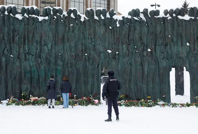A police officer stands guard as people lay flowers at the Wall of Grief monument to the victims of political repressions to honour the memory of Russian opposition leader Alexei Navalny in Moscow, Russia on February 17, 2024. (Photo by Reuters/Stringer)