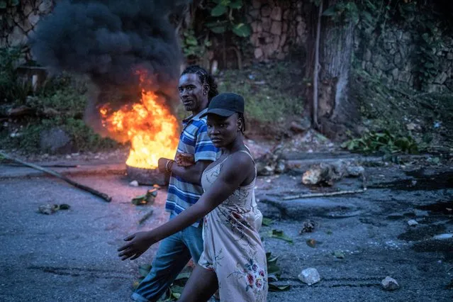 A couple walks past a burning roadblock set up to protest against a recent kidnapping and shooting in the Petionville neighborhood of Port-au-Prince, Haiti on November 1, 2021. (Photo by Adrees Latif/Reuters)