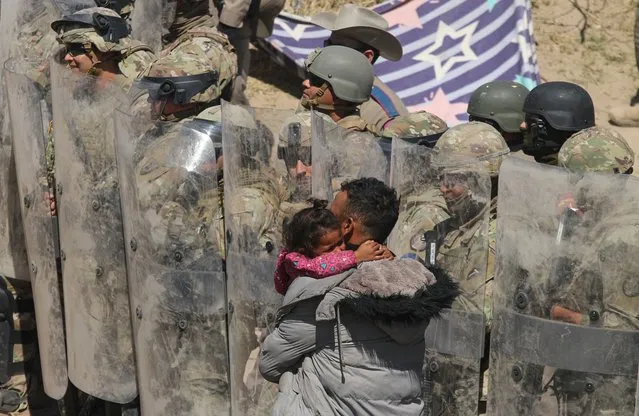 A Venezuelan migrant man carries one of his daughters while being forced to retreat by anti-riot members of the Texas National Guard and highway police who stand guard on the banks of the Rio Grande river to prevent the arrival of migrant people to the US, as seen from Ciudad Juarez, Chihuahua state, Mexico on March 22, 2024. (Photo by Herika Martinez/AFP Photo)