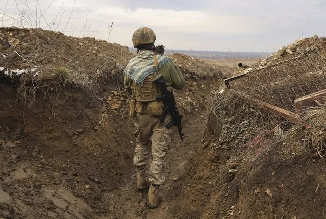 A Ukrainian soldier holds a cat and walks in a trench on the line of separation from pro-Russian rebels near Debaltsevo, Donetsk region, Ukraine, Ukraine Friday, December3, 2021. In this Friday, the Ukrainian defense minister warned that Russia could invade his country next month. Russia-West tensions escalated recently with Ukraine and its Western backers becoming increasingly concerned that a Russian troop buildup near the Ukrainian border could signal Moscow's intention to invade. (Photo by Andriy Dubchak/AP Photo)