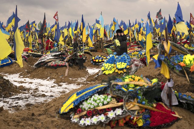 A woman adjusts her hood as she walks between the graves of soldiers, during the funeral of Hennadii Kovshyk, who was killed on the frontline in eastern Ukraine, in Kharkiv, Ukraine, Thursday, February 16, 2023. Russia again pummeled Ukraine with a barrage of cruise and other missiles on Thursday, hitting targets from east to west as the war 's one-year anniversary nears, one of the strikes killed a 79-year-old woman and injured at least seven other people, Ukrainian authorities said. (Photo by Vadim Ghirda/AP Photo)