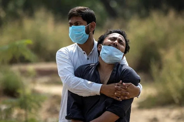 A man is consoled by his relative as he sees the body of his father, who died from the coronavirus disease (COVID-19), before his burial at a graveyard in New Delhi, India, April 16, 2021. (Photo by Danish Siddiqui/Reuters)