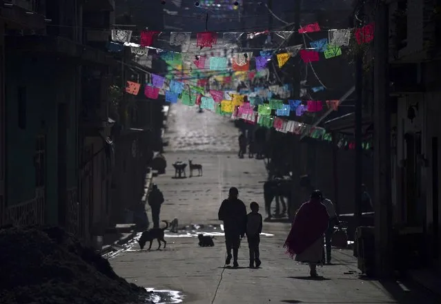 Pedestrians walk under colored banners left over from Christmas celebrations in the Puerpecha Indigenous community of Comachuen, Mexico, Wednesday, January 19, 2022. According to Porfirio Gabriel, the organizer of migrant workers from Comachuen, the town would be “dead” without remittances. The money migrants send home to their relatives are expected to top $50 billion for the first time in 2021. (Photo by Fernando Llano/AP Photo)