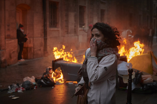 A woman runs past a burning barricade holding a scarf to her face during demonstrations in central Paris against the French Government's Pension Law ahead of a final decision on the law by French lawmakers on April 14, 2023 in Paris, France. After three months of nationwide strikes and protests against the French Government's plans to raise the minimum pension age from 62 to 64, the ruling by France's highest constitutional court means that the Government can pass the law as early as next week. (Photo by Kiran Ridley/Getty Images)