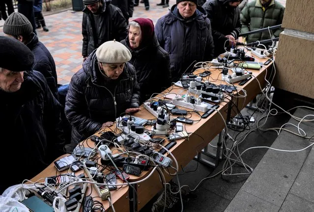 People charge their cellphones in a public building in Bucha, northwest of Kyiv, on April 6, 2022, during Russia's military invasion launched on Ukraine. Western powers were readying new sanctions against Russia after Ukraine's president called for tougher action and accused Moscow of atrocities during the six-week war. The measures follow an international outcry over hundreds of civilians found dead in areas from which Russian troops have withdrawn around Ukraine's capital, including the town of Bucha. (Photo by Ronaldo Schemidt/AFP Photo)