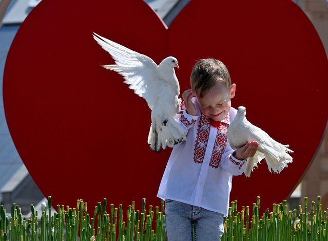 A boy wearing a Vyshyvanka, a traditional Ukrainian embroidered blouse, holds pigeons as he poses for his mother at Independence Square in Kyiv during “Vyshyvanka Day” on May 18, 2023, amid the Russian invasion of Ukraine. Vyshyvanka Day, is an annual celebration of Ukrainian folk traditions where Ukrainians wear much-loved traditional embroidered clothing known as a “Vyshyvanka”. This year's celebration is being viewed as a symbol of national unity against Russia's invasion. (Photo by Sergei Supinsky/AFP Photo)