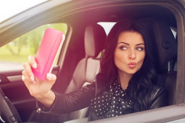 Beautiful brunette woman doing selfie in the car. Lips young woman taking selfie picture with smart phone camera outdoors in car. (Photo by  Ekaterina Demidova/Alamy Stock Photo)