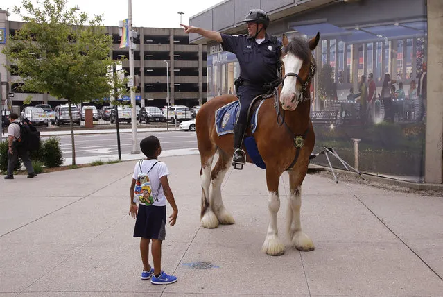 Chaz Samuel, 6, of Virginia, whose mother is attending the National Governor's Association meeting, asks Providence mounted police office Dan Famigliette where the nearest park is that he and his brother can play in accompanied by their nanny during the first day of the National Governor's Association meeting Thursday, July 13, 2017, in Providence, R.I. Officer Famigliette and his Clydesdale “Charlie” are posted along the perimeter of the NGA meeting. (Photo by Stephan Savoia/AP Photo)