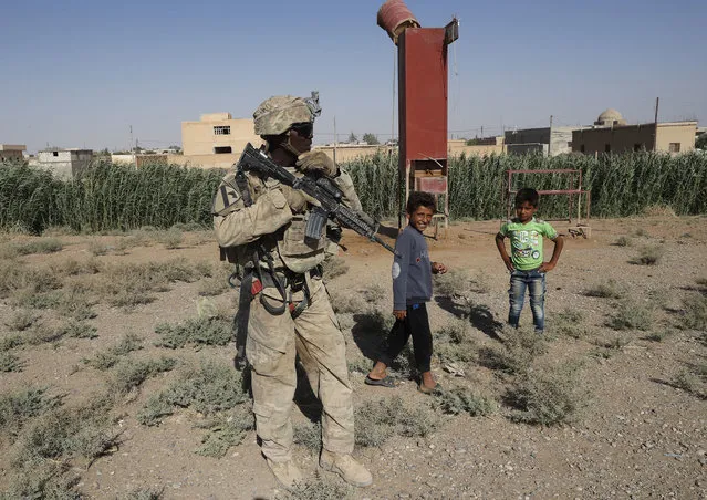 A U.S. soldier stands near Syrian children on a road that links to Raqqa, Syria, Wednesday, July 26, 2017. The U.S. has up to 1,000 troops in Syria mostly involved in training and advising the local forces against IS. Kurdish forces have gained confidence in light of open U.S. support to their forces, particularly as the battle for Raqqa took off. (Photo by Hussein Malla/AP Photo)