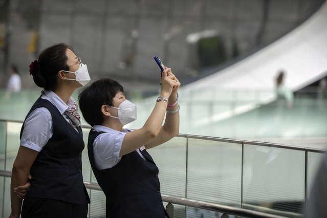 A woman wearing a face mask takes a photo at a shopping and office complex in Beijing, Thursday, June 30, 2022. (Photo by Mark Schiefelbein/AP Photo)