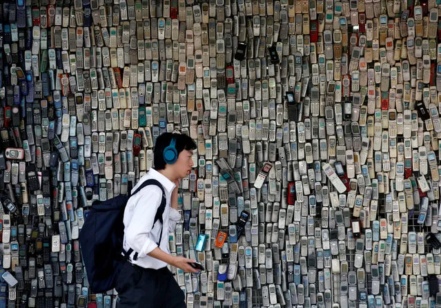 A man using a smartphone walks past an electronic shop's wall decorated with old cell phones which its owner Watanabe Masanao had collected over 20 years is pictured in Tokyo, Japan July 5, 2017. (Photo by Kim Kyung-Hoon/Reuters)