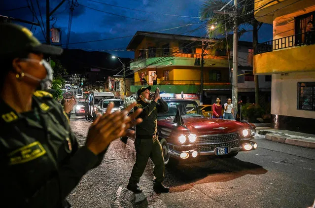 A police officer sings as a hearse drives along a street as part of a campaign sponsored by the Colombian police and a funerary home to raise awareness during the new coronavirus pandemic in Envigado, Antioquia, Colombia, on April 1, 2020. More than 20,000 cases of COVID-19 were registered in Latin America and the Caribbean by Wednesday, according to an AFP tally using information provided by national health authorities and the World Health Organization. (Photo by Joaquin Sarmiento/AFP Photo)