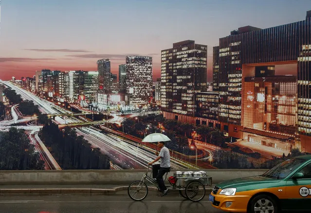 A man rides a tricycle past an advertising poster showing a night-time city view at the construction site of an apartment tower in Beijing, July 19, 2016. (Photo by Thomas Peter/Reuters)