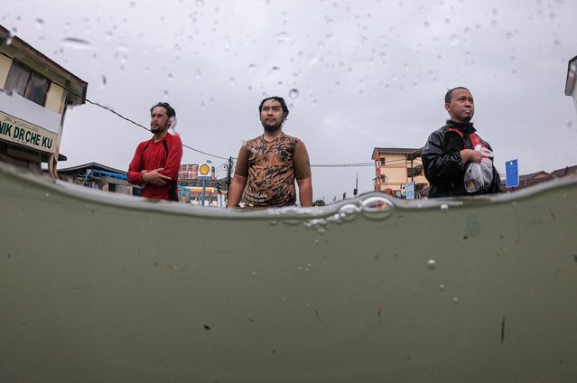 People wade through a flooded street during heavy rain in Pasir Puteh, in Malaysia's Kelantan state on November 30, 2024. (Photo by Mohd Rasfan/AFP Photo)
