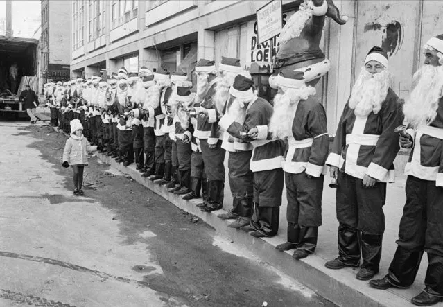 Robin Levy, 4, of Riverdale, Bronx, N.Y., walks in front of some 50 Santas on 48th Street and Eighth Avenue in New York City, November 23, 1962. The Santas are graduates of the Volunteers of America and will solicit funds from passersby during the holiday season. (Photo by AP Photo)