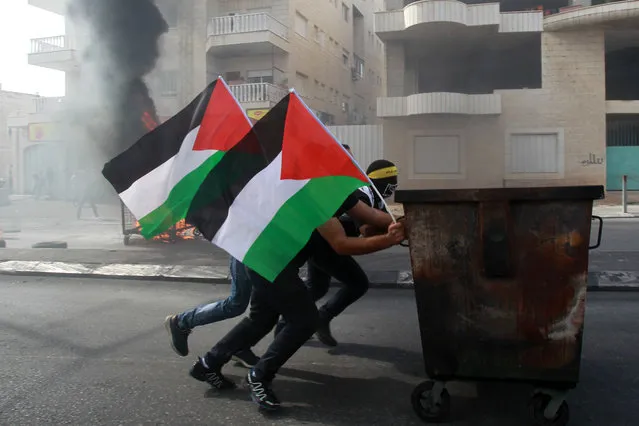 Palestinian protesters push a waste container during clashes with Israeli security forces on October 13, 2015 in the West Bank city of Bethlehem. A Palestinian was killed in the clashes, Palestinian medical sources said, the latest such incident in nearly two weeks of violence. (Photo by Musa Al-Shaer/AFP Photo)