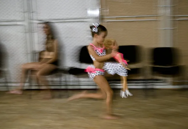 In this September 10, 2016 picture, Denisa Maria Preda, 6 years-old, runs holding a doll, before competing in the children category of the Romania Miss Pole Dance Contest, ahead of the finals of the Pole Sport&Fitness World Championship 2016 in Bucharest, Romania. Contestants from 12 countries, including China, Russia, Ukraine, Britain, Spain, Brazil, Italy and Romania took part in the finals held at the Children's Palace in south Bucharest, and, apart from their sports routine, they were also judged on their costumes, and entertainment value. (Photo by Vadim Ghirda/AP Photo)