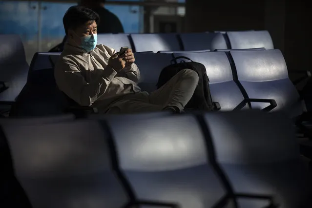 A traveler wearing a face mask to protect against the coronavirus sits at a boarding gate at the Shanghai Hongqiao International Airport in Shanghai, Friday, November 6, 2020. With the COVID-19 outbreak largely under control within its borders, air travel in China has mostly returned to pre-pandemic levels. (Photo by Mark Schiefelbein/AP Photo)