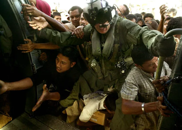 In this January 8, 2005 file photo, US Navy AW2 Maxwell Bjeule (no state given) tries to restrain a surging crowd of survivors as they struggle to get food and other supplies being unloaded from a US Navy Sea Hawk helicopter during its continuing sortie to the tsunami-stricken town of Meulaboh, southeast of Banda Aceh, the capital of Aceh province, in northwest Indonesia.  (Photo by Achmad Ibrahim/AP Photo)
