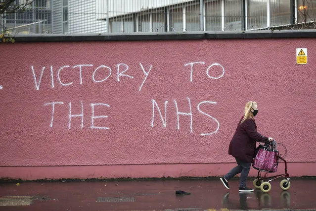 A woman walks past graffiti with the words Victory to the NHS (National Health Service) on a wall at the Royal Victoria Hospital, one of several hospitals around Britain that are handling the initial phase of a COVID-19 immunization program, in West Belfast, Northern Ireland, Tuesday, December 8, 2020. British health authorities rolled out the first doses of a widely tested and independently reviewed COVID-19 vaccine Tuesday, starting a global immunization program that is expected to gain momentum as more serums win approval. (Photo by Peter Morrison/AP Photo)