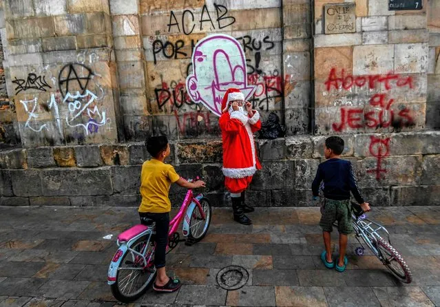 Venezuelan migrant boys look at a man dressed as Santa Claus in Bogota, Colombia on December 15, 2020. (Photo by Juan Barreto/AFP Photo)