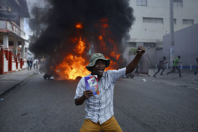 A protester kneels in front of a burning barricade with a copy of the Haitian Constitution during a demonstration demanding the resignation of President Jovenel Moise, in Port-au-Prince, Haiti, Friday, January 15, 2021. Moise has one more year in power, but a growing groundswell of opposition is organizing protests and demanding he resign next month amid spiraling crime, a crumbling economy and approval of what critics say are illegal presidential decrees and unconstitutional moves, worrying many that Moïse is amassing too much power as he enters his second year of rule by decree. (Photo by Joseph Odelyn/AP Photo)