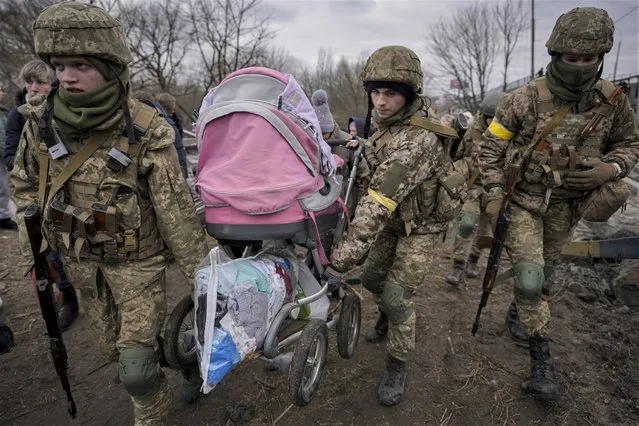Ukrainian servicemen carry a baby stroller after crossing the Irpin river on an improvised path under a bridge that was destroyed by a Russian airstrike, while assisting people fleeing the town of Irpin, Ukraine, Saturday, March 5, 2022. What looked like a breakthrough cease-fire to evacuate residents from two cities in Ukraine quickly fell apart Saturday as Ukrainian officials said shelling had halted the work to remove civilians hours after Russia announced the deal. (Photo by Vadim Ghirda/AP Photo)