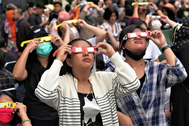People use protective glasses to watch solar eclipse in Jakarta, Indonesia, Thursday, April 20, 2023. The lucky few in the path of the hybrid solar eclipse would either get plunged into the darkness of a total eclipse or see a “ring of fire” as the sun peeks out from behind the moon. (Photo by Tatan Syuflana/AP Photo)