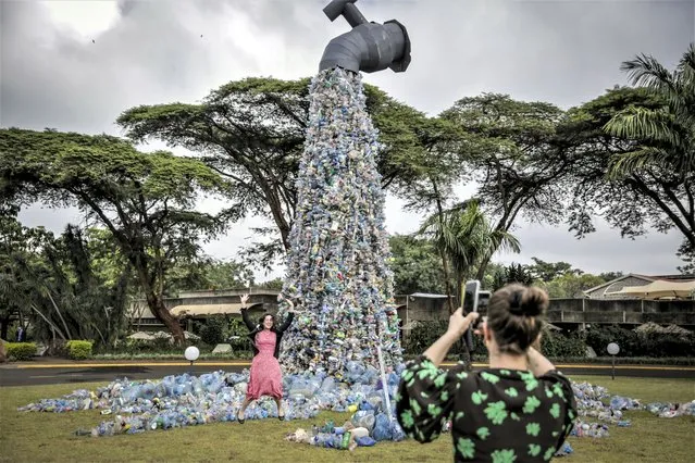 Delegates take photos of themselves in front of a giant art sculpture showing a tap outpouring plastic bottles, each of which was picked up in the neighborhood of Kibera, during the U.N. Environment Assembly (UNEA) held at the U.N. Environment Programme (UNEP) headquarters in Nairobi, Kenya Wednesday, March 2, 2022. Delegates met to discuss a binding international framework to address the growing problem of plastic waste in the world's oceans, rivers and landscape. (Photo by Brian Inganga/AP Photo)