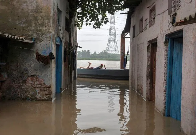 A man lies in a boat outside his house flooded with rising water levels after heavy monsoon rains on the banks of river Yamuna in New Delhi, India on July 11, 2023. (Photo by Adnan Abidi/Reuters)