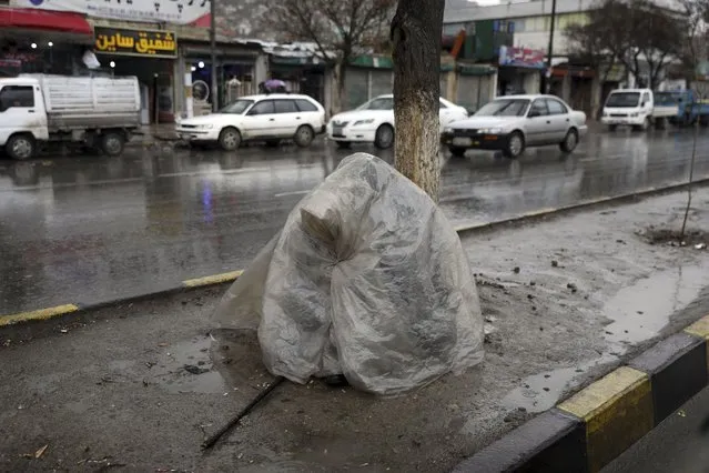 A homeless person covers herself with a plastic sheet in the rain on a sidewalk, in Kabul, Afghanistan, Monday, March 22, 2021. (Photo by Rahmat Gul/AP Photo)