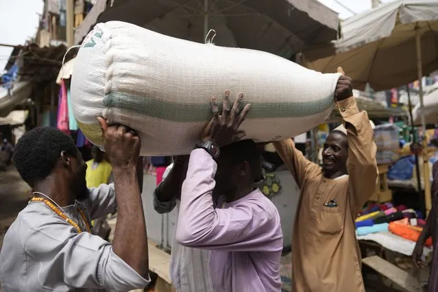 People balance a bag containing grains on a man's head at a market in Kano, Nigeria, Thursday, July 13, 2023. (Photo by Sunday Alamba/AP Photo)