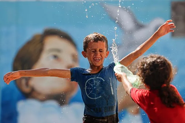 A girl splashes water over a boy amidst soaring temperatures at the Shati camp for Palestinian refugees in Gaza City on July 17, 2023. (Photo by Mohammed Abed/AFP Photo)