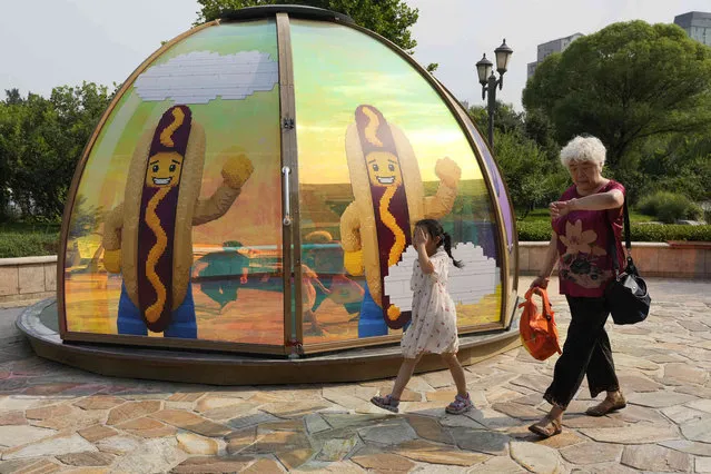 Residents walk past an advertisement depicting hot-dog character in the afternoon in Beijing, Thursday, July 20, 2023. (Photo by Ng Han Guan/AP Photo)