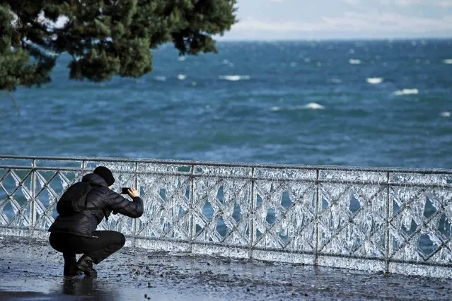 A man takes pictures of a frozen fence by the lake side due to the strong wind conditions in Geneva February 8, 2015. (Photo by Pierre Albouy/Reuters)