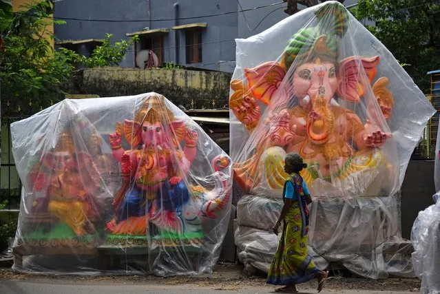 A woman walks in front of the idols of the Hindu god Ganesha, which are covered in plastic sheets to protect them from dust and rain, on a roadside ahead of the Ganesh Chaturthi festival, in Chennai, India on September 13, 2023. The Ganesh Chaturthi festival is a ten-day-long event that is one of the biggest Hindu festivals which is celebrated all over India. During the Ganpati festival, which is celebrated as the birthday of Lord Ganesha, idols of the Hindu deity are worshiped at hundreds of pandals or makeshift tents before they are immersed into water bodies. This year, the festival starts on 19 September 2023. (Photo by Idrees Mohammed/EPA/EFE)