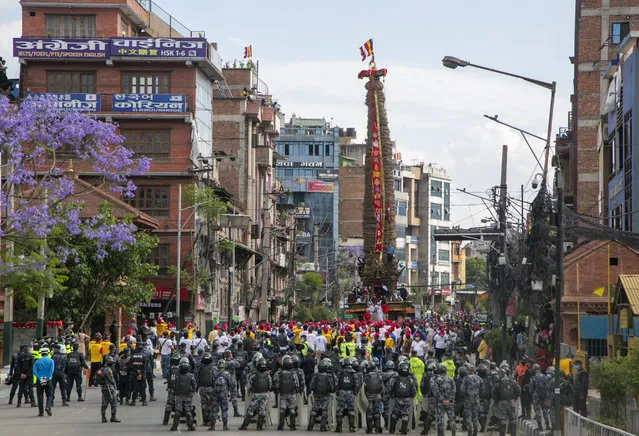 Policemen stand guard as Nepalese devotees pull a chariot during the Rato Machindranath chariot festival in Lalitpur, Nepal, Saturday, May 15, 2021. A truncated version of a Hindu chariot festival took place in Nepal's capital on Saturday amid strict COVID-19 restrictions, following an agreement between organizers and authorities that prevented a repeat of violent confrontations between police and protesters at last year's festival. (Photo by Niranjan Shrestha/AP Photo)