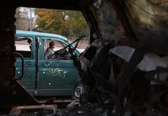 A child sits in a destroyed car next to destroyed Russian military vehicles on display in front of Saint Michael's Golden-Domed Monastery in Kyiv on October 26, 2023, amid the Russian invasion of Ukraine. (Photo by Anatolii Stepanov/AFP Photo)