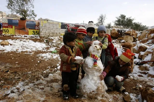 Young Syrian refugees build a snowman following a storm in a makeshift refugee camp in the Lebanese village of Baaloul in the Bekaa Valley, on December 12, 2013. The UNHCR has prepared stockpiles of items including plastic sheeting, floor mats, blankets and mattresses to help refugees whose shelters might be flooded or destroyed by the storm. (Photo by Mahmoud Zayyat/AFP Photo)