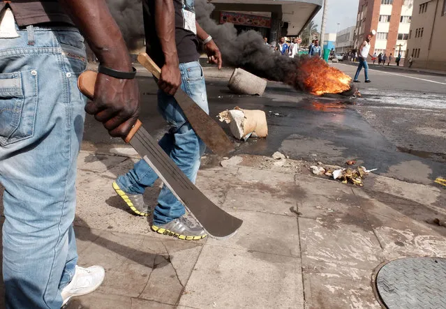 In this photo taken Tuesday, April 14, 2015, immigrant men armed with machetes make their way onto a Durban, South Africa, street during clashes with police and in search of locals that attacked foreign shop owners in the city center. (Photo by Tebogo Letsie/AP Photo)