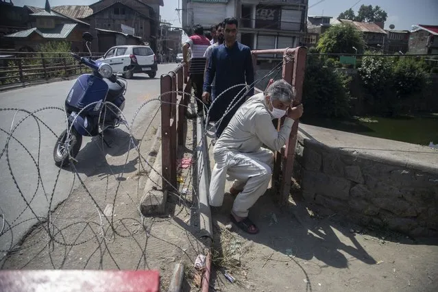 Kashmiri civilians cross a barricade set up by the police in Srinagar, Indian controlled Kashmir, Thursday, September 2, 2021. Indian authorities cracked down on public movement and imposed a near-total communications blackout Thursday in disputed Kashmir after the death of Syed Ali Geelani, a top separatist leader who became the emblem of the region’s defiance against New Delhi. Geelani, who died late Wednesday at age 92, was buried in a quiet funeral organized by authorities under harsh restrictions, his son Naseem Geelani told The Associated Press. He said the family had planned the burial at the main martyrs’ graveyard in Srinagar, the region’s main city, as per his will but were disallowed by police. (Photo by Mukhtar Khan/AP Photo)