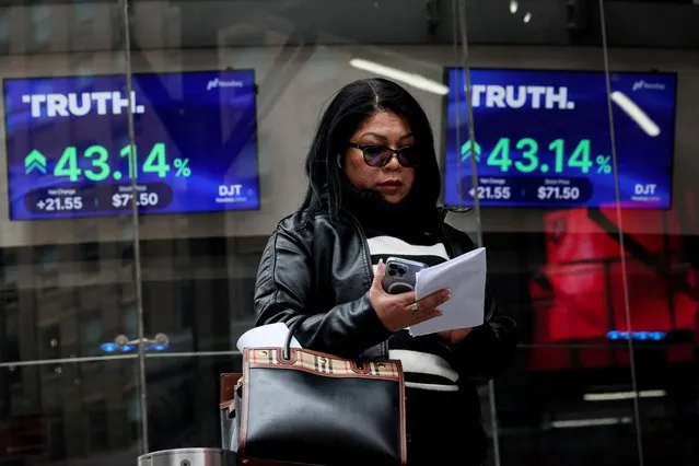A woman uses her phone in front of screens displaying trading information about shares of Truth Social and Trump Media & Technology Group, outside the Nasdaq Market site in New York City on March 26, 2024. (Photo by Brendan McDermid/Reuters)