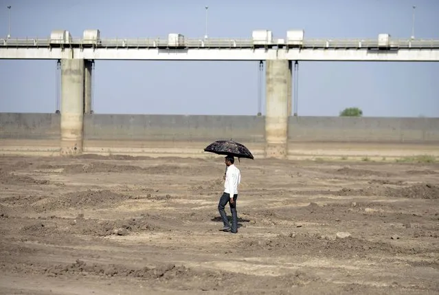 An Indian man holds an umbrella as he walks on the dry reservoir bed next to Gunda Dam by Gunda village in Botad district, some 150 km from Ahmedabad in India's western Gujarat state, on April 1, 2016. Vast regions of western India have been facing acute water shortages due to drought conditions. (Photo by Sam Panthaky/AFP Photo)