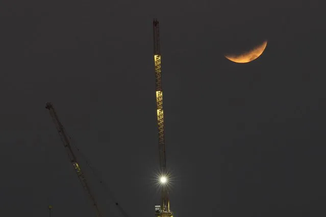 A partial lunar eclipse is seen behind a crane in Manila, Philippines on Friday, November 19, 2021. (Photo by Aaron Favila/AP Photo)